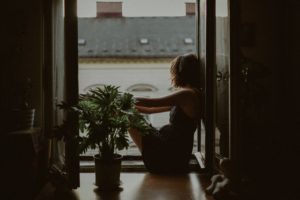 woman sitting on floor looking out doors of a balcony thinking (image on Acceptance | Making Peace With Your Past)