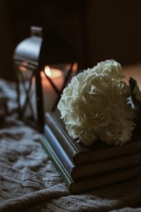 stack of three brown books with a boquet of white flowers sitting on top in front of a lit brown iron and glasshurricane candle