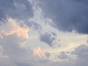 above head view of white and grayish blue clouds parting revealing the moon in daytime sky