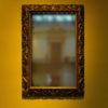 a blurry mirror in an ornate gold frame on on golden yellow wall