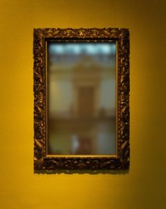 a blurry mirror in an ornate gold frame on on golden yellow wall