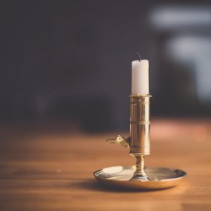 white unlit candle in an old fashioned gold candle stick holder with a handle sitting on a wooden table